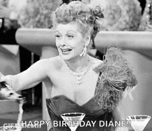 A Black And White Photo Of A Woman In A Dress Sitting At A Table With Two Martini Glasses And A Necklace . GIF