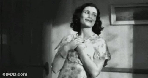 A Black And White Photo Of A Woman In A Floral Dress Standing In A Hallway . GIF