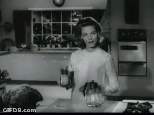 A Black And White Photo Of A Woman In A Kitchen Holding A Bottle GIF