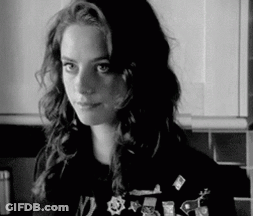 A Black And White Photo Of A Woman In A Kitchen Wearing A Sweater With Pins On It . GIF