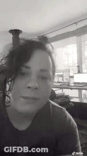 A Black And White Photo Of A Woman In A Living Room With A Laptop On A Desk . GIF