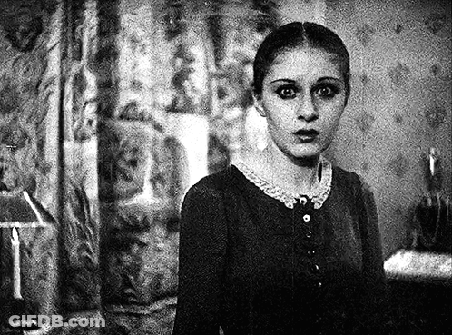 A Black And White Photo Of A Woman In A Room With A Lamp In The Background . GIF