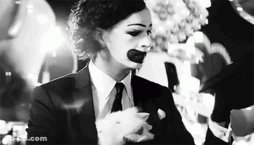 A Black And White Photo Of A Woman In A Suit And Tie With A Clown Makeup On Her Face . GIF