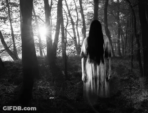 A Black And White Photo Of A Woman In A White Dress Standing In The Woods . GIF