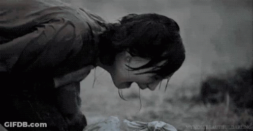 A Black And White Photo Of A Woman Kneeling Down With Her Head On A Dead Body . GIF