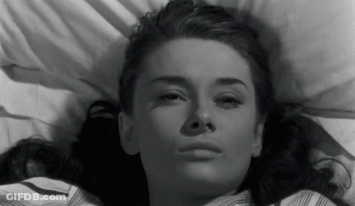 A Black And White Photo Of A Woman Laying In Bed Looking At The Camera . GIF