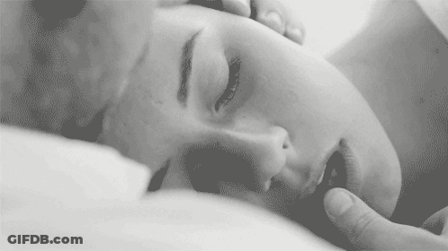 A Black And White Photo Of A Woman Laying On A Bed With Her Eyes Closed And A Man Touching Her Face . GIF