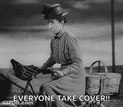 A Black And White Photo Of A Woman Riding A Bicycle With The Words Everyone Take Cover ! GIF