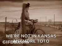 A Black And White Photo Of A Woman Riding A Bike With The Caption We 'Re Not In Kansas Anymore Toto . GIF