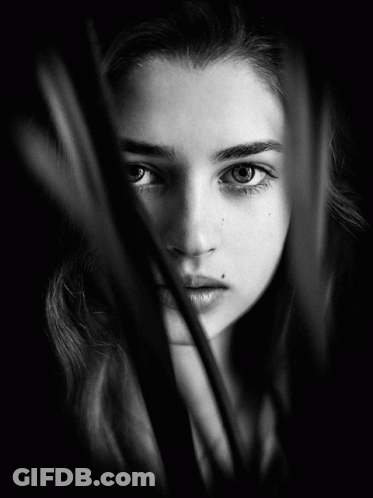 A Black And White Photo Of A Woman 'S Face Behind A Few Leaves GIF
