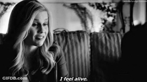 A Black And White Photo Of A Woman Saying `` I Feel Alive '' While Sitting On A Couch . GIF