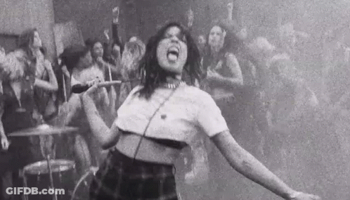 A Black And White Photo Of A Woman Singing Into A Microphone In Front Of A Crowd Of People . GIF