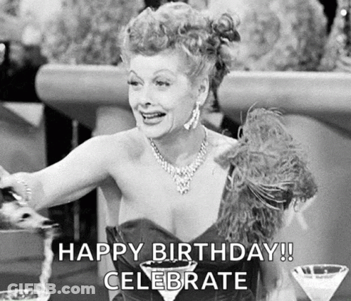 A Black And White Photo Of A Woman Sitting At A Table With A Martini Glass And A Feather Boa . GIF