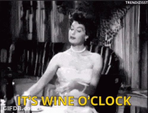 A Black And White Photo Of A Woman Sitting At A Table With The Words " It 'S Wine O ' Clock " GIF