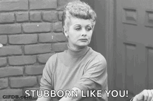 A Black And White Photo Of A Woman Sitting In Front Of A Brick Wall Saying `` Stubborn Like You '' . GIF