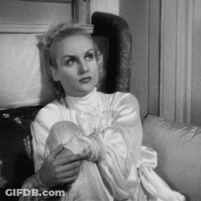 A Black And White Photo Of A Woman Sitting On A Couch With Her Legs Crossed . GIF