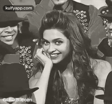 A Black And White Photo Of A Woman Smiling While Sitting In A Crowd Of People . GIF