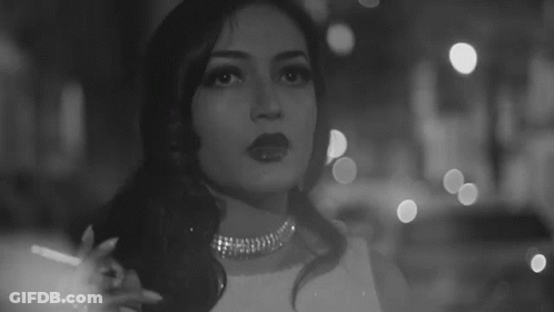 A Black And White Photo Of A Woman Smoking A Cigarette In A Dark Room . GIF