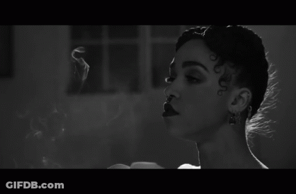 A Black And White Photo Of A Woman Smoking A Cigarette In A Room . GIF