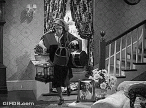 A Black And White Photo Of A Woman Standing In A Living Room Holding A Birdcage . GIF