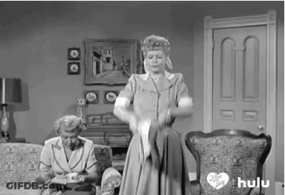 A Black And White Photo Of A Woman Standing In A Living Room Holding A Cat . GIF