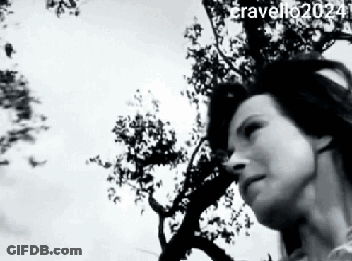 A Black And White Photo Of A Woman Standing In Front Of A Tree . GIF