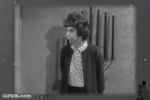 A Black And White Photo Of A Woman Standing In Front Of A Wall With Candles On It . GIF