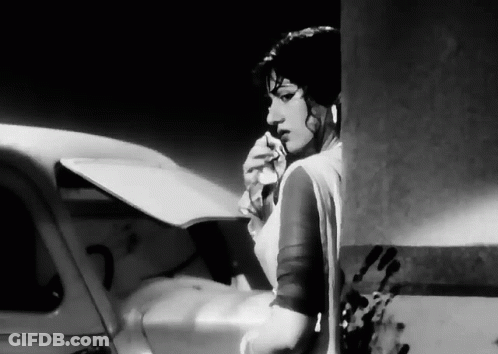 A Black And White Photo Of A Woman Standing Next To A Car Holding A Piece Of Paper . GIF