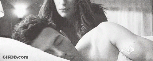 A Black And White Photo Of A Woman Standing Next To A Man Laying In Bed . GIF
