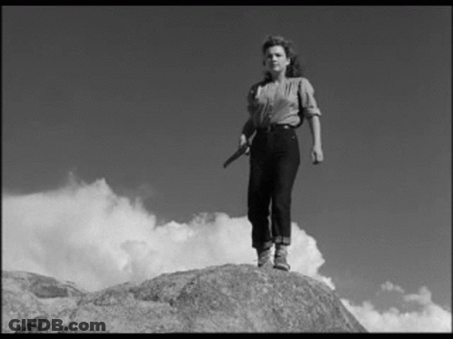 A Black And White Photo Of A Woman Standing On A Rock Holding A Knife . GIF
