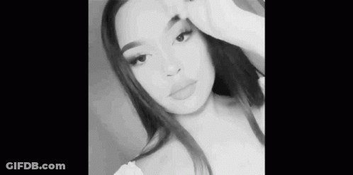 A Black And White Photo Of A Woman Taking A Selfie With Her Hand On Her Face . GIF