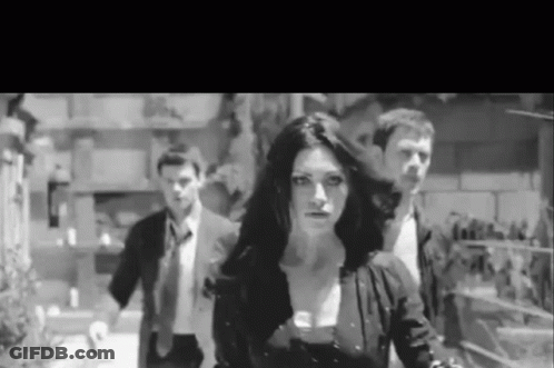 A Black And White Photo Of A Woman Walking With Two Men In Suits . GIF