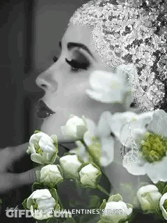 A Black And White Photo Of A Woman Wearing A Hat And Flowers . GIF