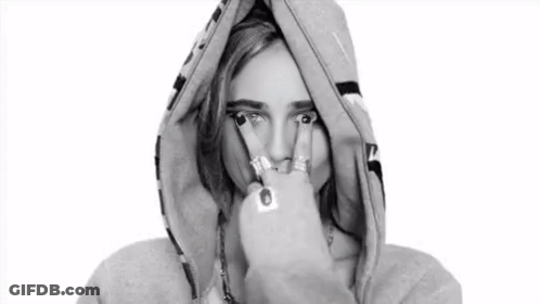 A Black And White Photo Of A Woman Wearing A Hoodie And Making A Peace Sign . GIF