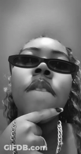 A Black And White Photo Of A Woman Wearing Sunglasses And A Silver Chain GIF