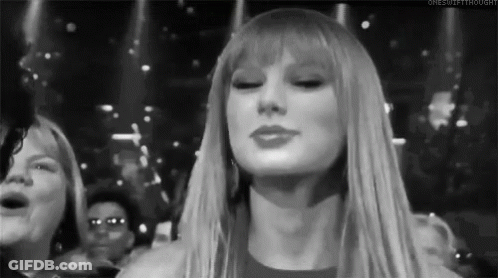 A Black And White Photo Of A Woman With Long Blonde Hair And Bangs Standing In Front Of A Crowd . GIF