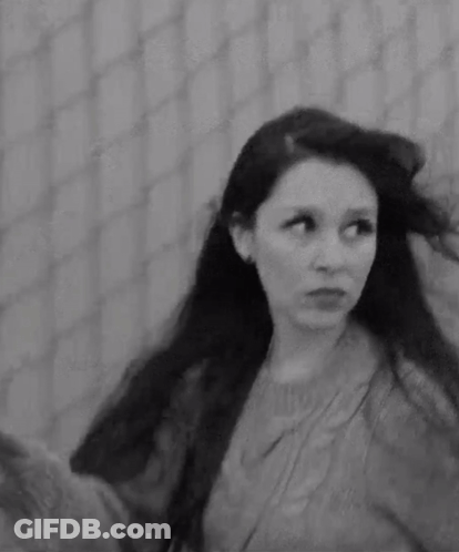 A Black And White Photo Of A Woman With Long Hair In Front Of A Fence . GIF