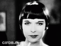A Black And White Photo Of A Woman With Short Hair Looking At The Camera . GIF