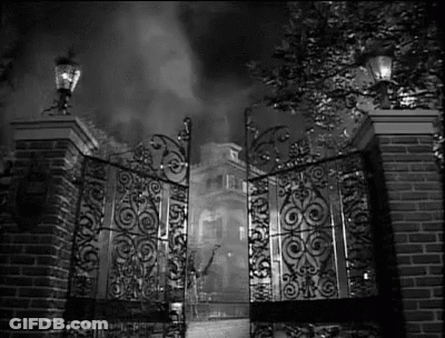 A Black And White Photo Of A Wrought Iron Gate Leading To A Mansion . GIF