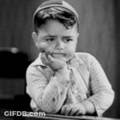 A Black And White Photo Of A Young Boy Sitting At A Desk With His Hand On His Chin . GIF