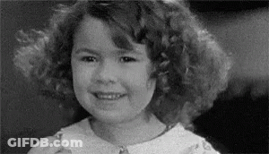 A Black And White Photo Of A Young Girl With Curly Hair Smiling . GIF