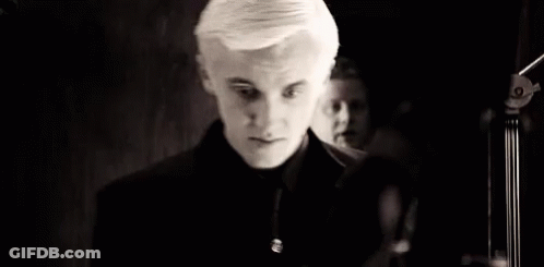 A Black And White Photo Of A Young Man In A Black Suit And Tie . GIF