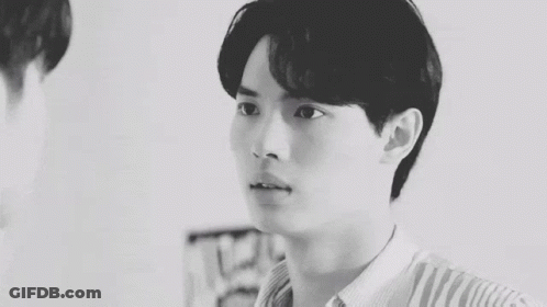 A Black And White Photo Of A Young Man In A Plaid Shirt Looking Over His Shoulder . GIF