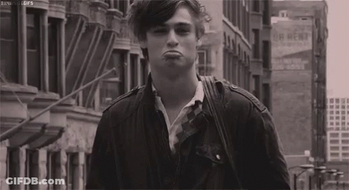 A Black And White Photo Of A Young Man Making A Funny Face While Walking Down A City Street . GIF