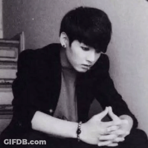 A Black And White Photo Of A Young Man Sitting Down With His Hands Folded And A Bracelet On His Wrist . GIF