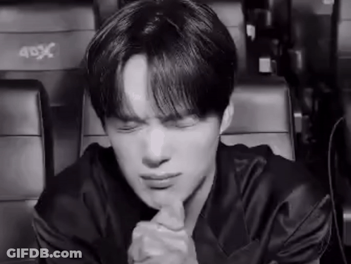 A Black And White Photo Of A Young Man Sitting In A Theater With His Eyes Closed And His Hands Folded . GIF