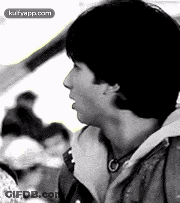 A Black And White Photo Of A Young Man Talking To Someone In A Crowd . GIF