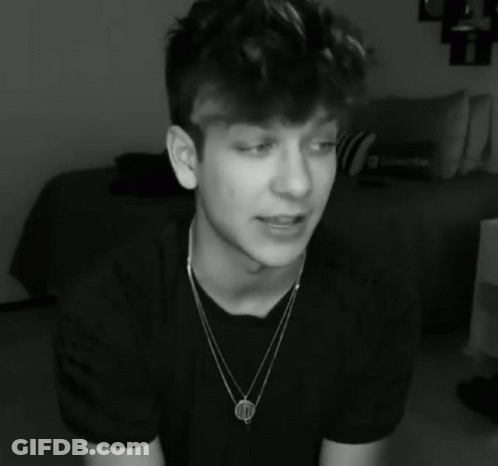 A Black And White Photo Of A Young Man Wearing A Necklace That Has The Letter M On It GIF