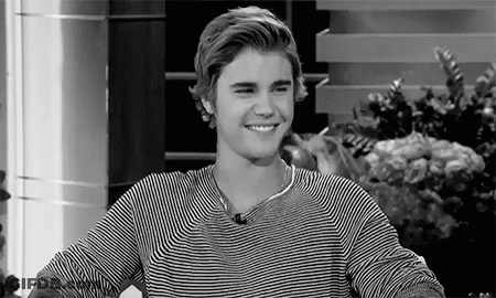 A Black And White Photo Of A Young Man Wearing A Striped Shirt Smiling . GIF