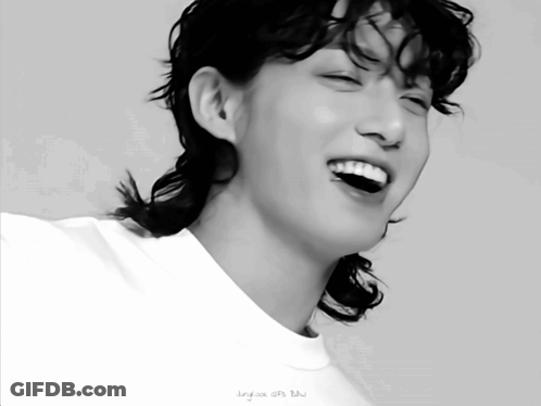 A Black And White Photo Of A Young Man With A Ponytail Smiling GIF